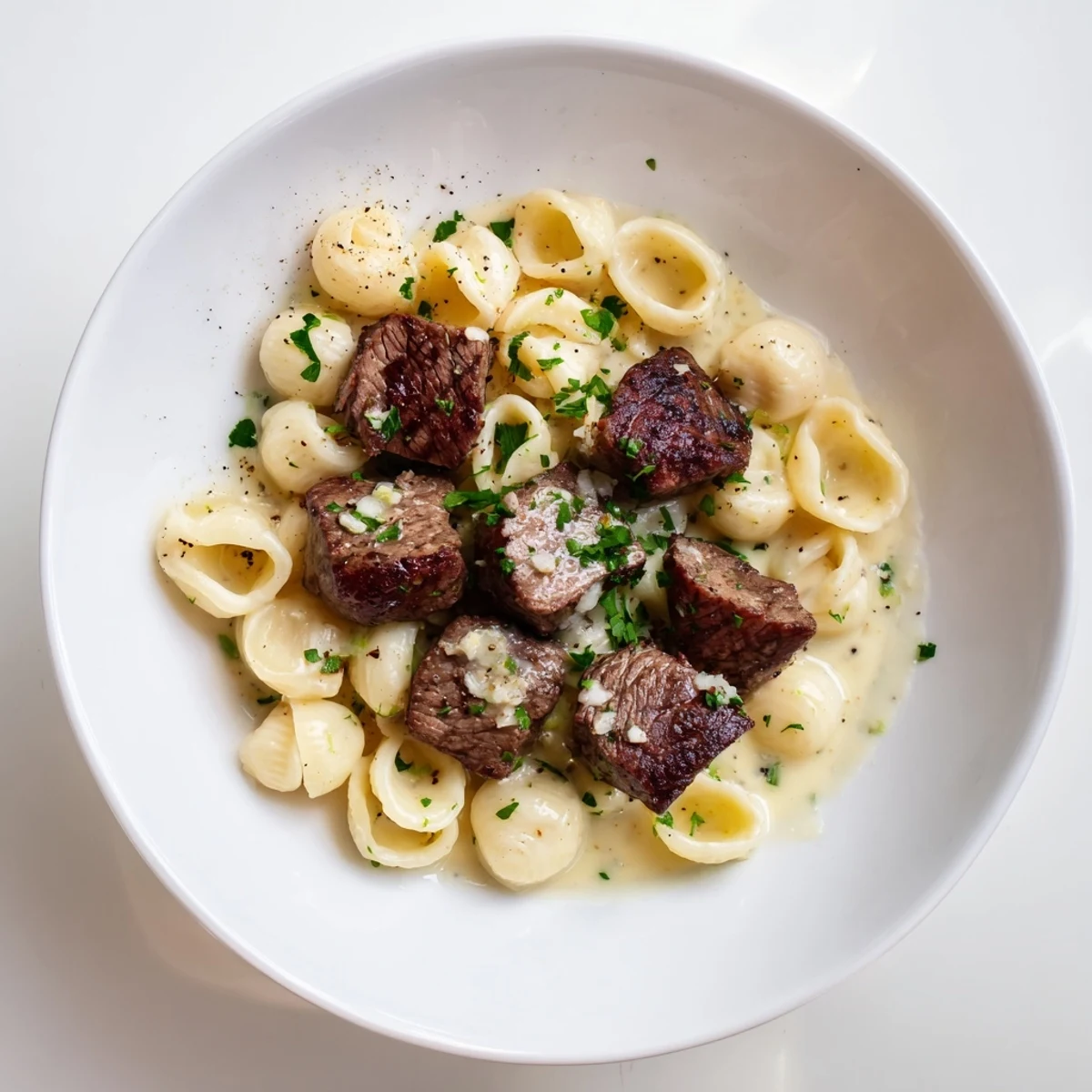 Golden-brown garlic butter steak bites served atop creamy, cheesy shells, an inviting, savory meal.