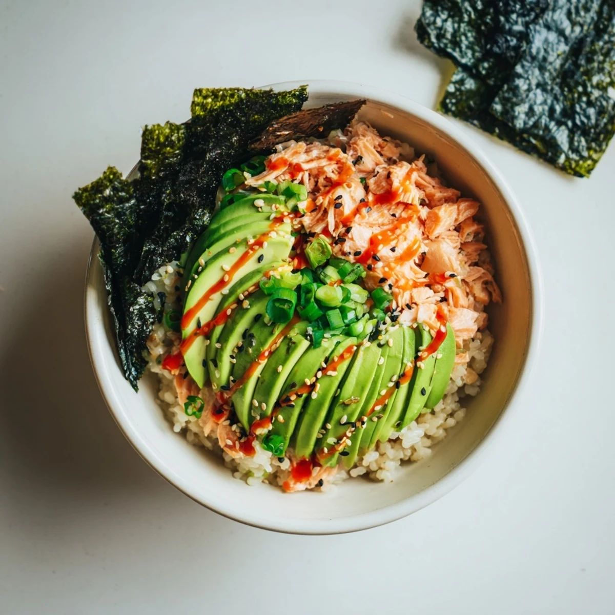 Flaked salmon and seasoned rice topped with creamy avocado and spicy mayo, ready to scoop into roasted nori sheets for a savory, sushi-inspired bowl.