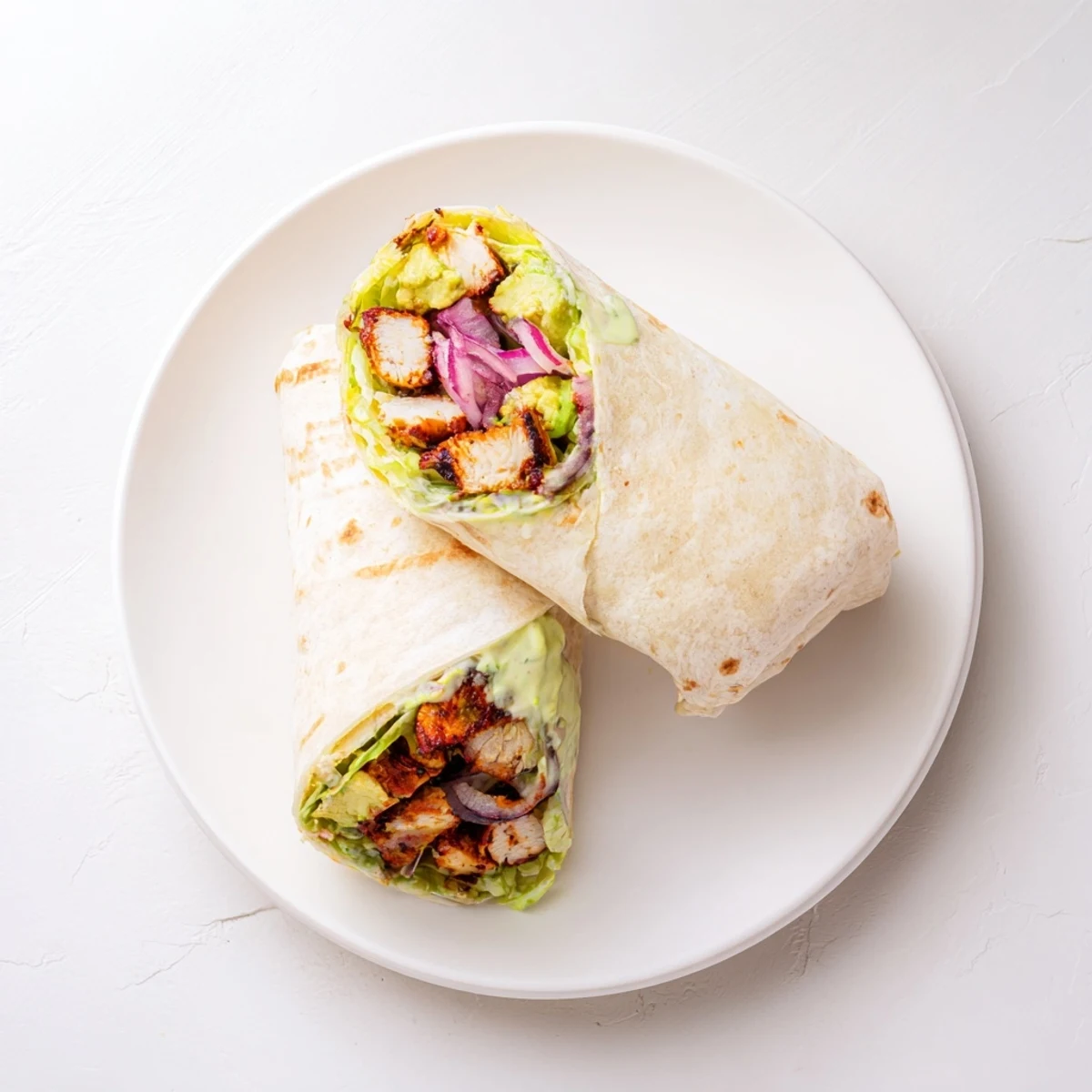 Sliced Smoky Chipotle Chicken Wrap filled with creamy avocado, crisp lettuce, and a tangy yogurt sauce on a wooden board.