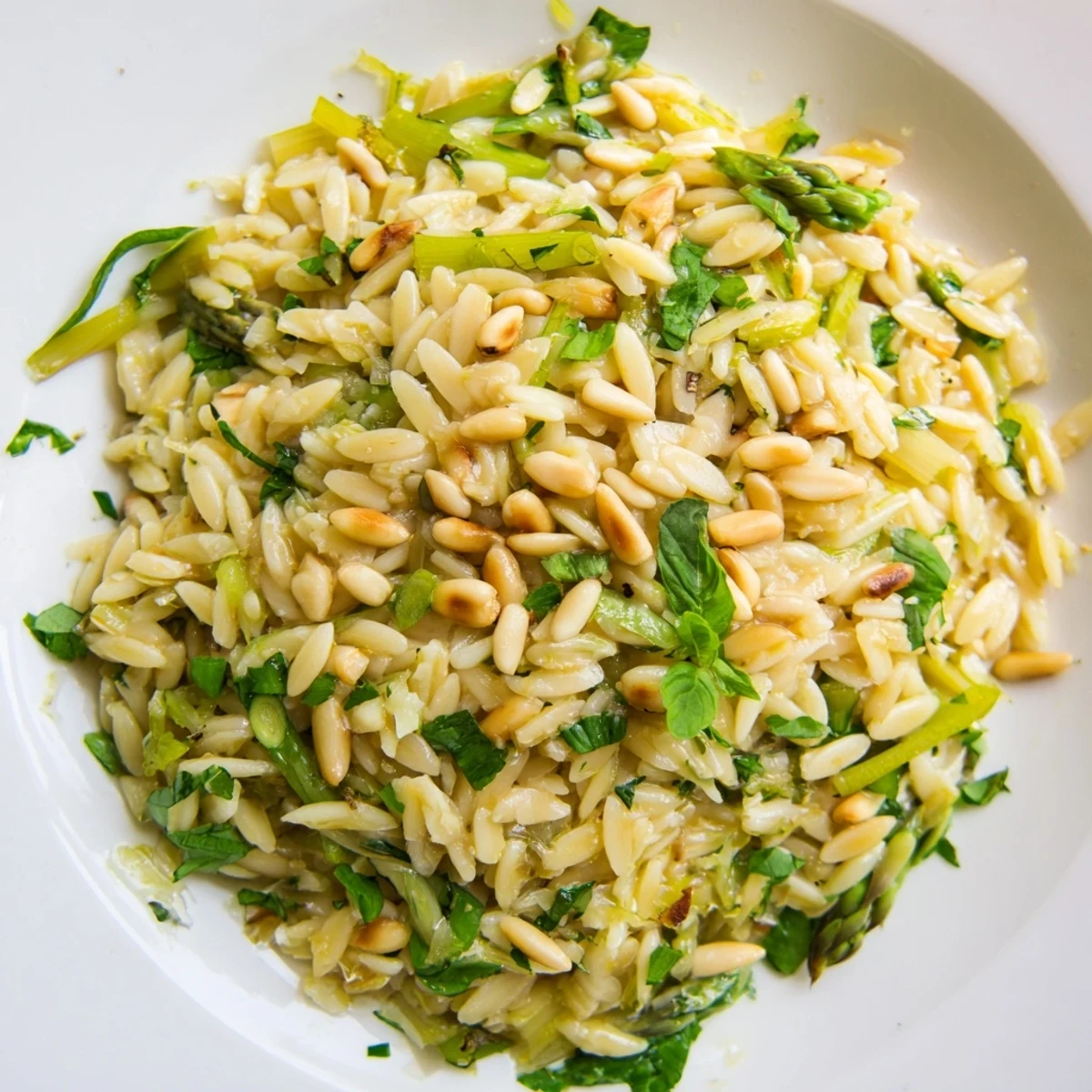 Fresh Asparagus Lemon Orzo Salad with shaved greens, grated Parmesan, and lemon vinaigrette, garnished with basil and parsley for a spring meal.  