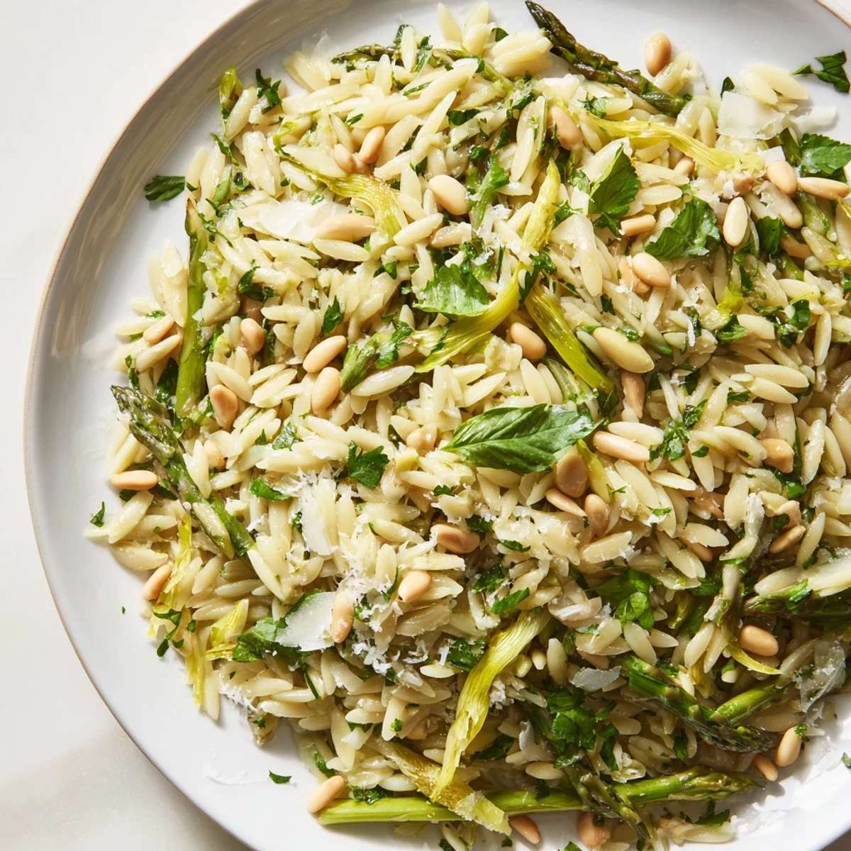A vibrant bowl of spring Asparagus Lemon Orzo Salad, featuring shaved asparagus and pine nuts tossed in a zesty lemon dressing.