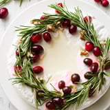 Festive Brie cheese appetizer boasts a fresh rosemary circle, sprinkled with optional ruby cranberries.
