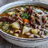 Black-Eyed Pea Stew with Smoked Ham Hocks simmering in a pot, rich broth with tender vegetables.