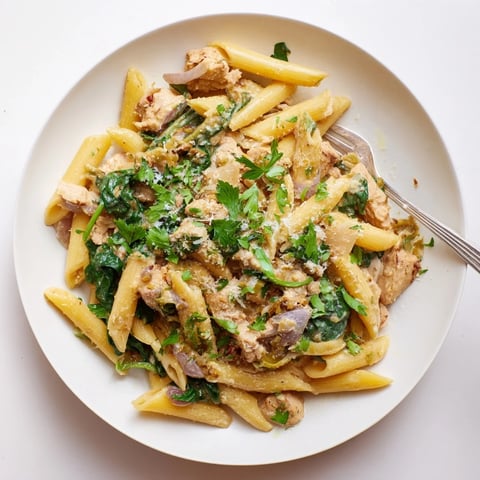A steaming bowl of one-pot creamy spinach & turkey Christmas pasta with fresh parsley garnish.