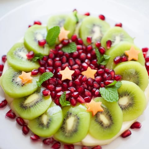 Bright, colorful Christmas wreath fruit plate with kiwi, pomegranate, and fresh mint, ready to serve.
