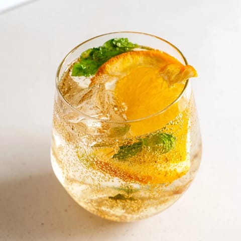 Colorful glass filled with sparkling probiotic soda mocktail garnished with orange slices and mint.  