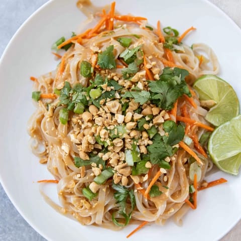 Tender rice noodles coated in spicy peanut sauce, topped with fresh cilantro and lime, ready to eat!