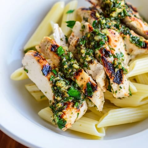 A bowl of Chimichurri Chicken Pasta features al dente noodles, savory chicken, and a drizzle of vibrant green sauce, ready to serve.