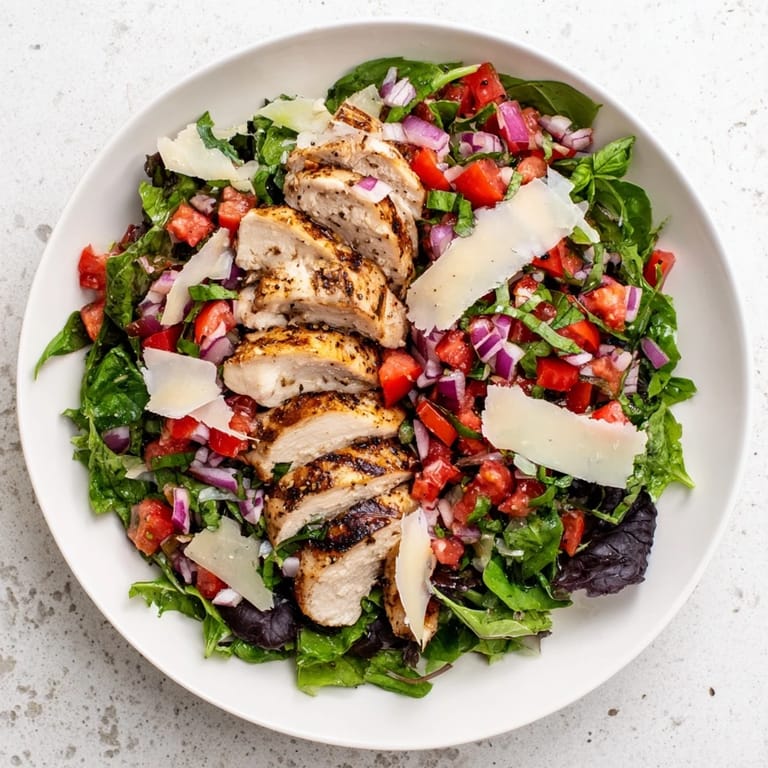 Sliced Bruschetta Chicken Salad served with lemon wedges and shaved Parmesan on greens.