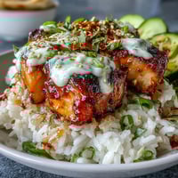 A colorful rice bowl with tender salmon cubes, creamy spicy mayo drizzle, crisp cucumber, and toasted sesame seeds for a satisfying meal.  